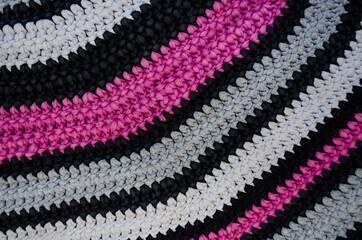 Close up of colorful knitted carpet in magenta, gray, black and white stripes.