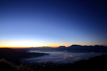 日の出前の阿蘇の雲海に透けて見える阿蘇の街の夜景