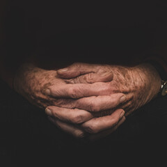 Intertwined hands of an elderly woman in the middle of a black background.