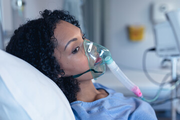 Worried african american female patient in hospital bed with oxygen ventilator