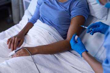 Midsection of caucasian female doctor in hospital vaccinating african american female patient