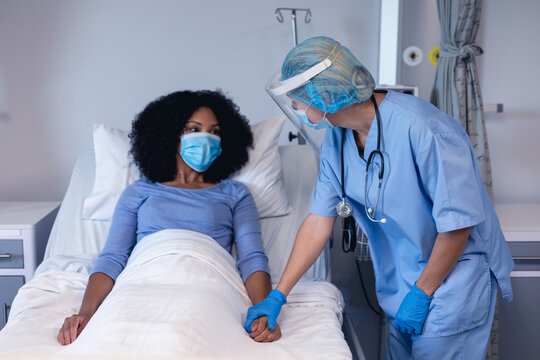 Caucasian Female Doctor In Hospital In Face Mask Consoling Female Patient In Bed Wearing Face Mask