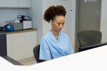 African american female receptionist sitting at desk using computer at hospital reception