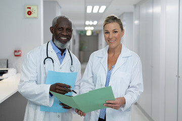 Portrait of diverse male and female doctors standing in hospital corridor smiling to camera