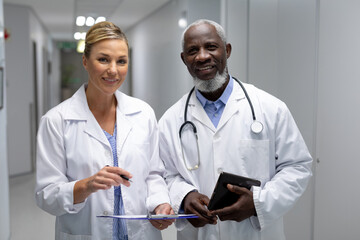 Portrait of diverse male and female doctors standing in hospital corridor smiling to camera