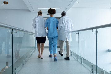 Three diverse male and female doctors walking through hospital corridor talking