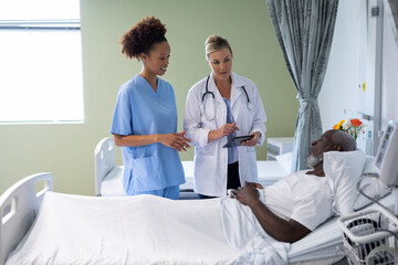 Two diverse female doctors and african american male patient in hospital room talking