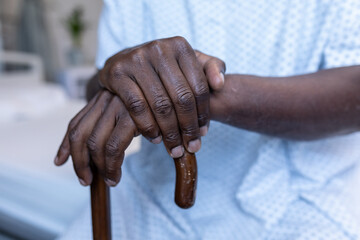 Fototapeta premium Midsection of african american male patient sitting on hospital bed holding cane
