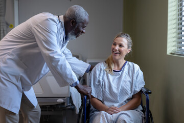 Obraz premium Diverse male doctor and female patient sitting on wheelchair smiling to each other