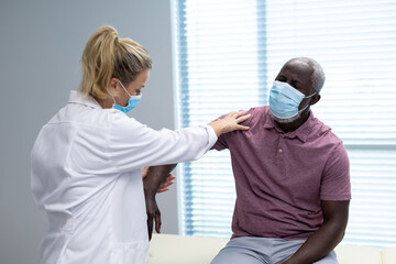 Caucasian female physiotherapist wearing mask stretching arm of african american male patient