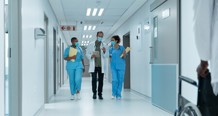 Diverse group of male and female doctors wearing face masks walking looking at tablet