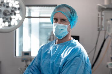 Fototapeta na wymiar Portrait of caucasian male doctor standing in operating theatre wearing face mask