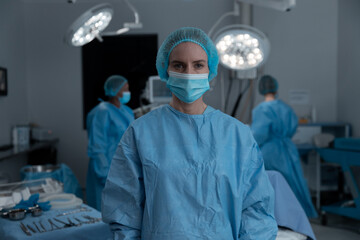 Portrait of caucasian female surgeon wearing face mask, surgical cap and gown in operating theatre