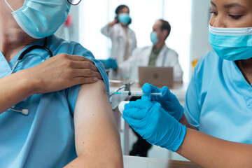 African american female doctor giving covid vaccination to male colleague, both in face masks