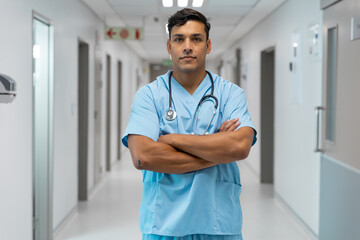 Portrait of mixed race male doctor smiling and standing in hospital corridor