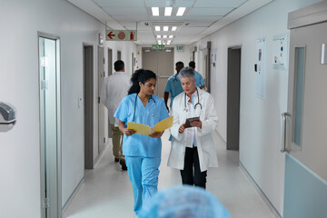Diverse male and female doctors walking through hospital corridor discussing