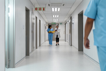 Diverse couple of female doctors walking through hospital corridor discussing