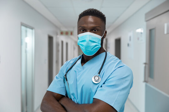 Portrait of african american male doctor wearing face mask standing in hospital corridor