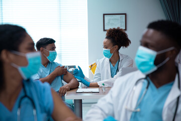 Obraz premium Mixed race couple of doctors wearing face masks making injection