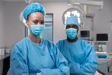 Diverse male and female surgeons wearing face masks and protective clothing in operating theatre