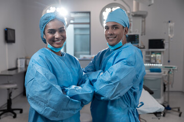 Smiling diverse male female surgeons with face masks and protective clothing in operating theatre