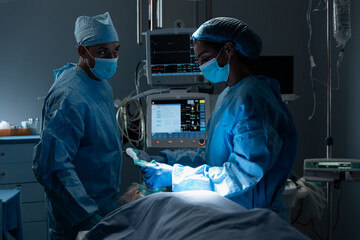 Diverse surgeons with face masks and protective clothing during operation, sedating patient