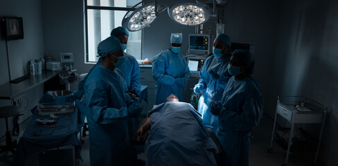 Diverse male and female doctors wearing face masks and surgical overalls in operating theatre