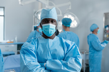 African american male surgeon with face mask and protective clothing in operating theatre
