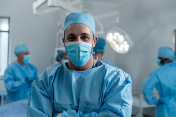 Fototapeta na wymiar Portrait of caucasian male surgeon wearing face mask and protective clothing in operating theatre