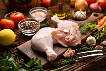 Fresh raw chicken thighs with ingredients for cooking on a wooden cutting board