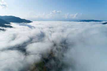 Aerial view drone shot of flowing fog waves on mountain tropical rainforest,Bird eye view image over the clouds Amazing nature background with clouds and mountain peaks in Nan Thailand