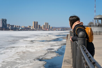 a girl stands on the embankment and looks at the city on the other side and at the ice on the river