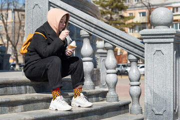 Girl eating ice cream on the city street. Teenager girl eating ice cream in a waffle cone sitting...