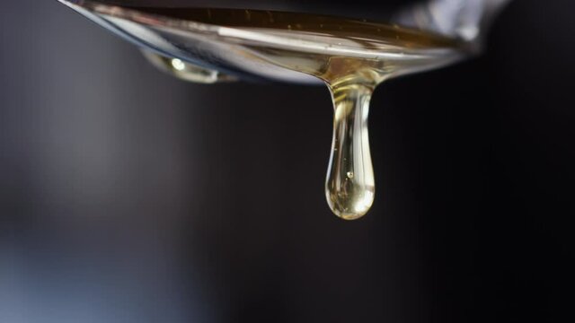 Close up shot of a drop of honey dripping from a silver spoon