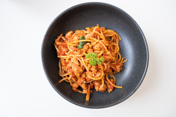 Top view of plate with spaghetti in tomato sauce and basil on white background