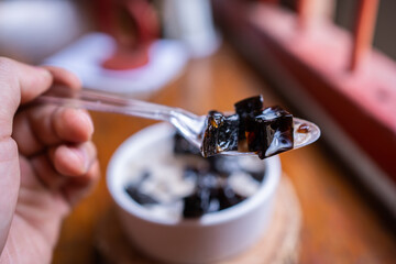 Grass jelly dessert herbal gelatin or jelly black with pineapple, syrup, ice, and brown sugar on the wooden background. Chinese style.