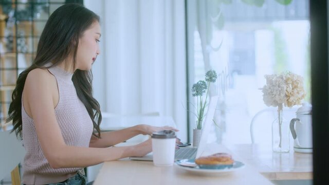 young attractive asian female wear casual cloth hand use smartphone and laptop device comminication social contact in cafe restaruant sit at counter next to big window daylight