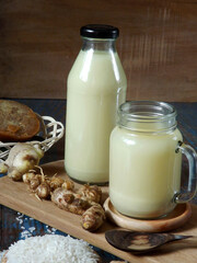A glass and bottle full of jamu beras kencur or Indonesian traditional herbal drink made from raw rice, kaempferia galanga, ginger, turmeric, and brown sugar. Low angle view with ingredients.
