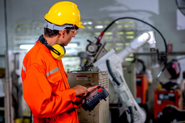 Factory worker man hold controller to control metal welding robotic machine and work in workplace...