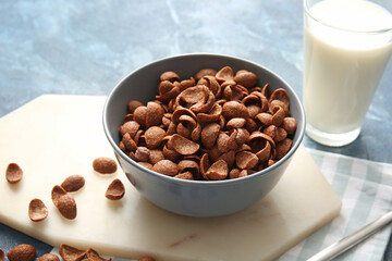 Bowl with chocolate cornflakes and glass of milk on color background