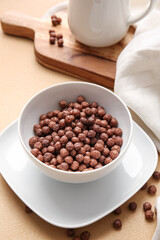 Bowl with chocolate corn balls on color background