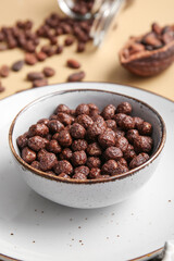 Bowl with chocolate corn balls on color background