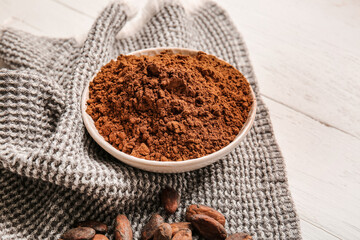 Bowl with cocoa powder on light wooden background