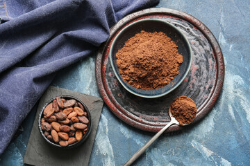 Bowls with cocoa powder and beans on color background