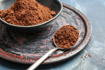 Bowl and spoon with cocoa powder on color background