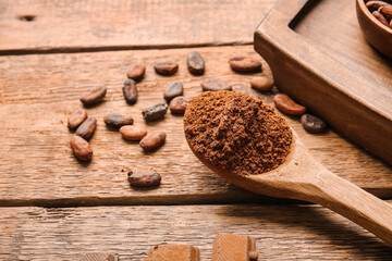 Spoon with cocoa powder on wooden background