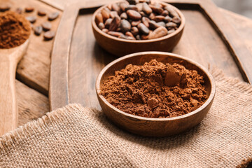 Bowls with cocoa powder and beans on wooden background