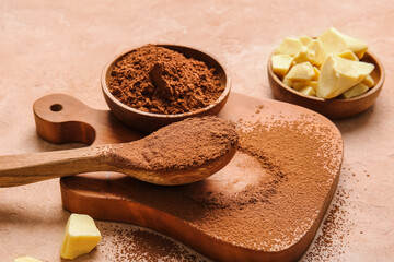 Bowls and spoon with cocoa powder and butter on color background