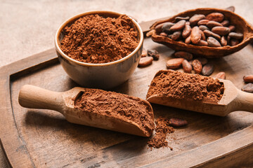 Bowl and scoops with cocoa powder and beans on wooden background