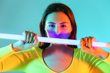 Toned portrait of beautiful young woman with neon lamp on color background